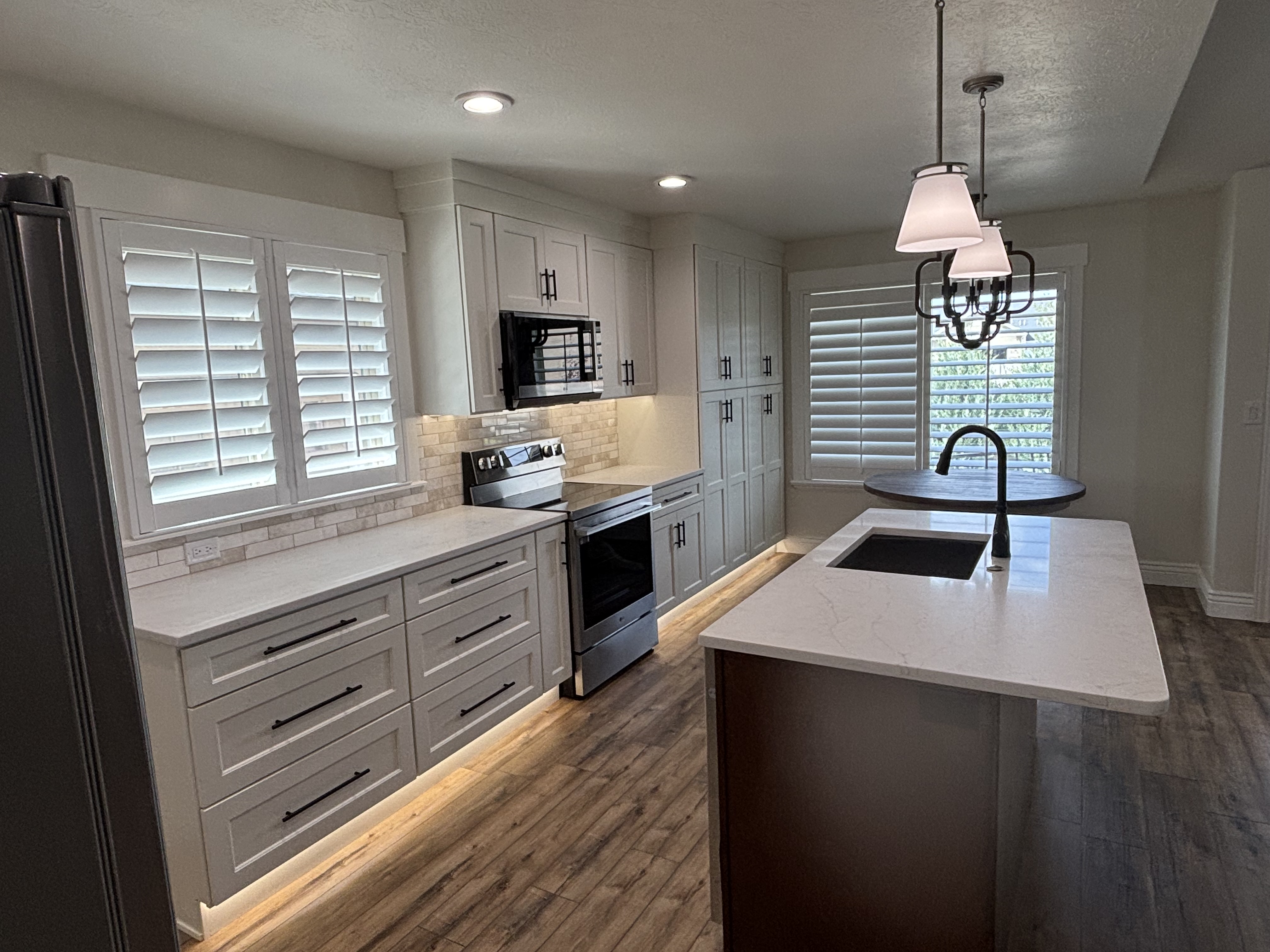 Modern kitchen renovation with white cabinets, stainless steel appliances, and stone backsplash